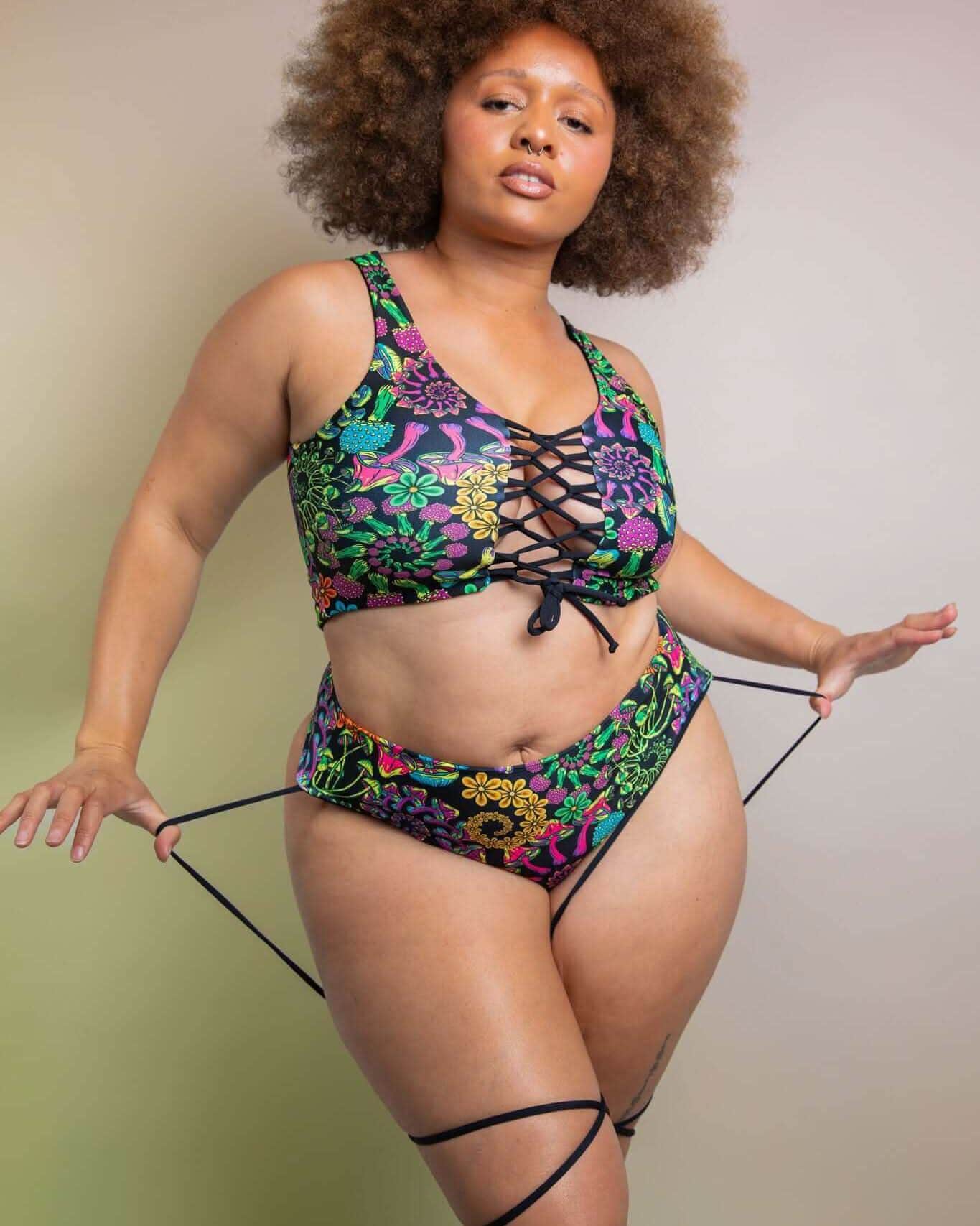 Model wearing PsyBloom strappy high waisted thong rave pants with vibrant floral print and matching top in confident pose