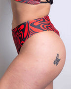 Red Void high waisted thong rave pants with swirling pattern, side view on model with butterfly tattoo