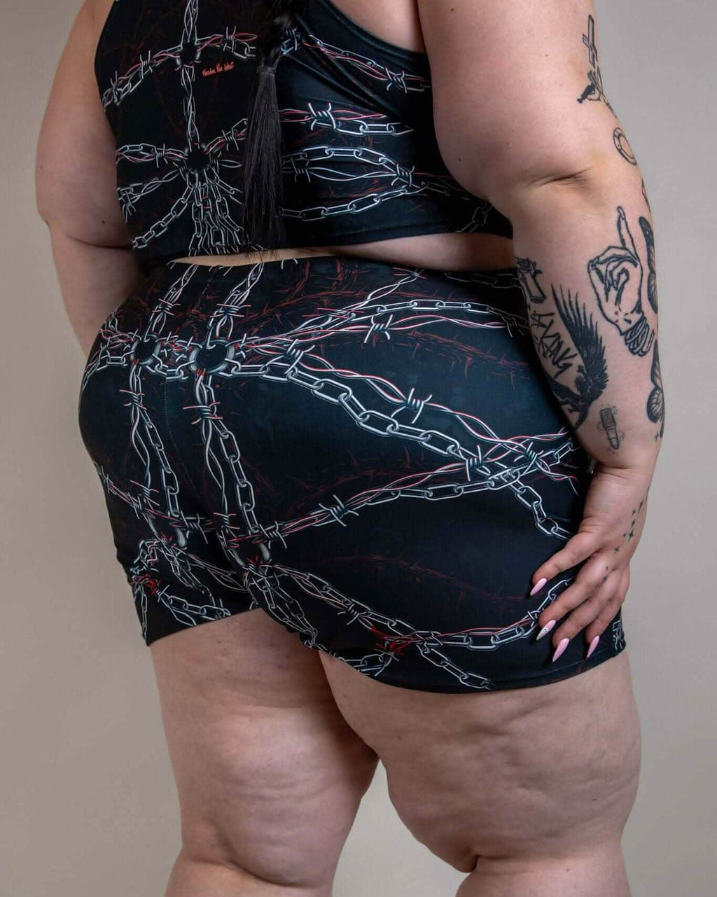 Plus-size model from back wearing Purgatory High Waist Shorts, black with white chains and red barbed wire, perfect for rave festivals.