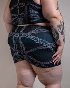 Plus-size model from back wearing Purgatory High Waist Shorts, black with white chains and red barbed wire, perfect for rave festivals.