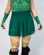 Model wearing emerald green mesh rave skirt with matching geometric top and neon leg wraps festival outfit