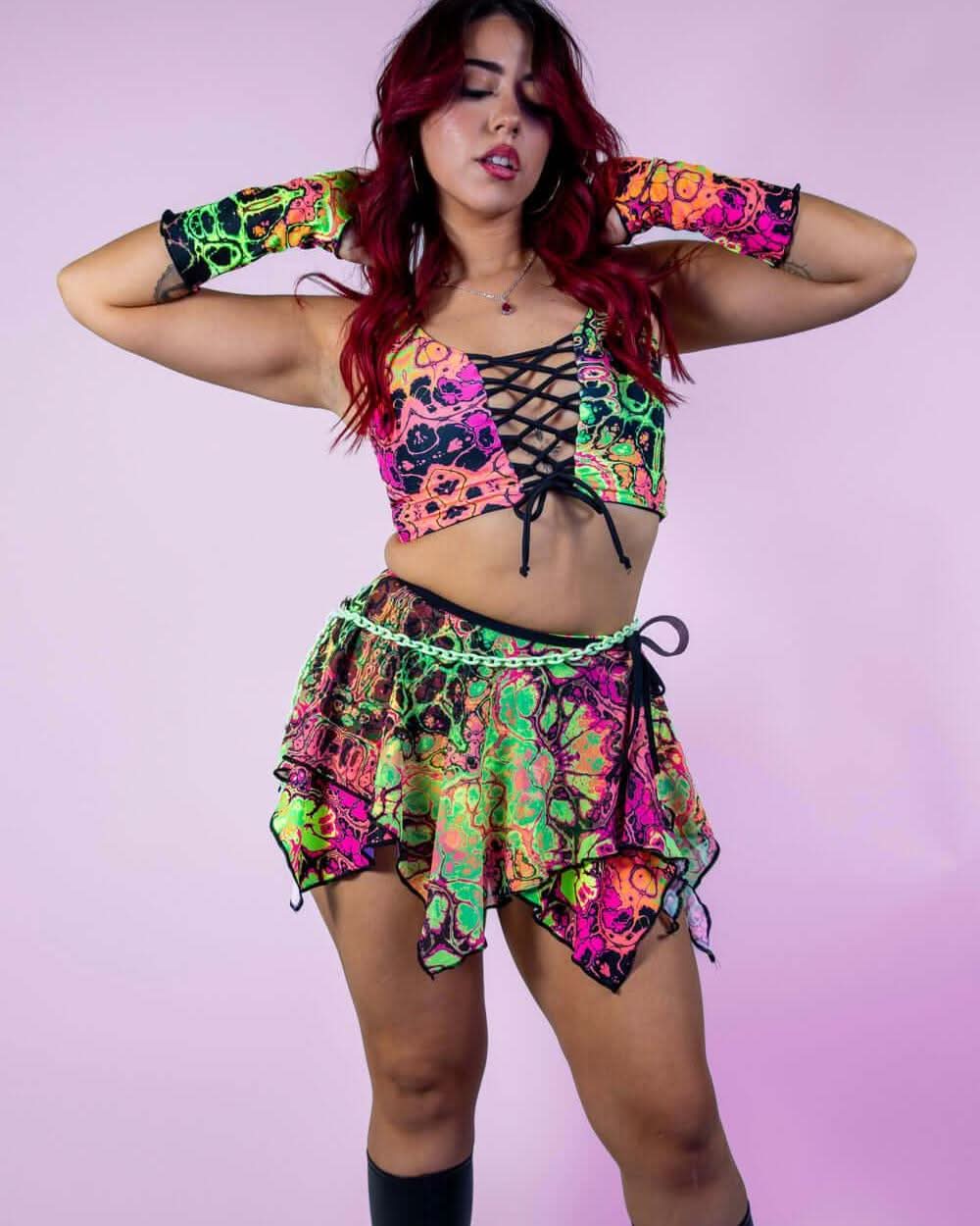Woman modeling Intensity psychedelic print rave skirt and top set in neon colors on pink background
