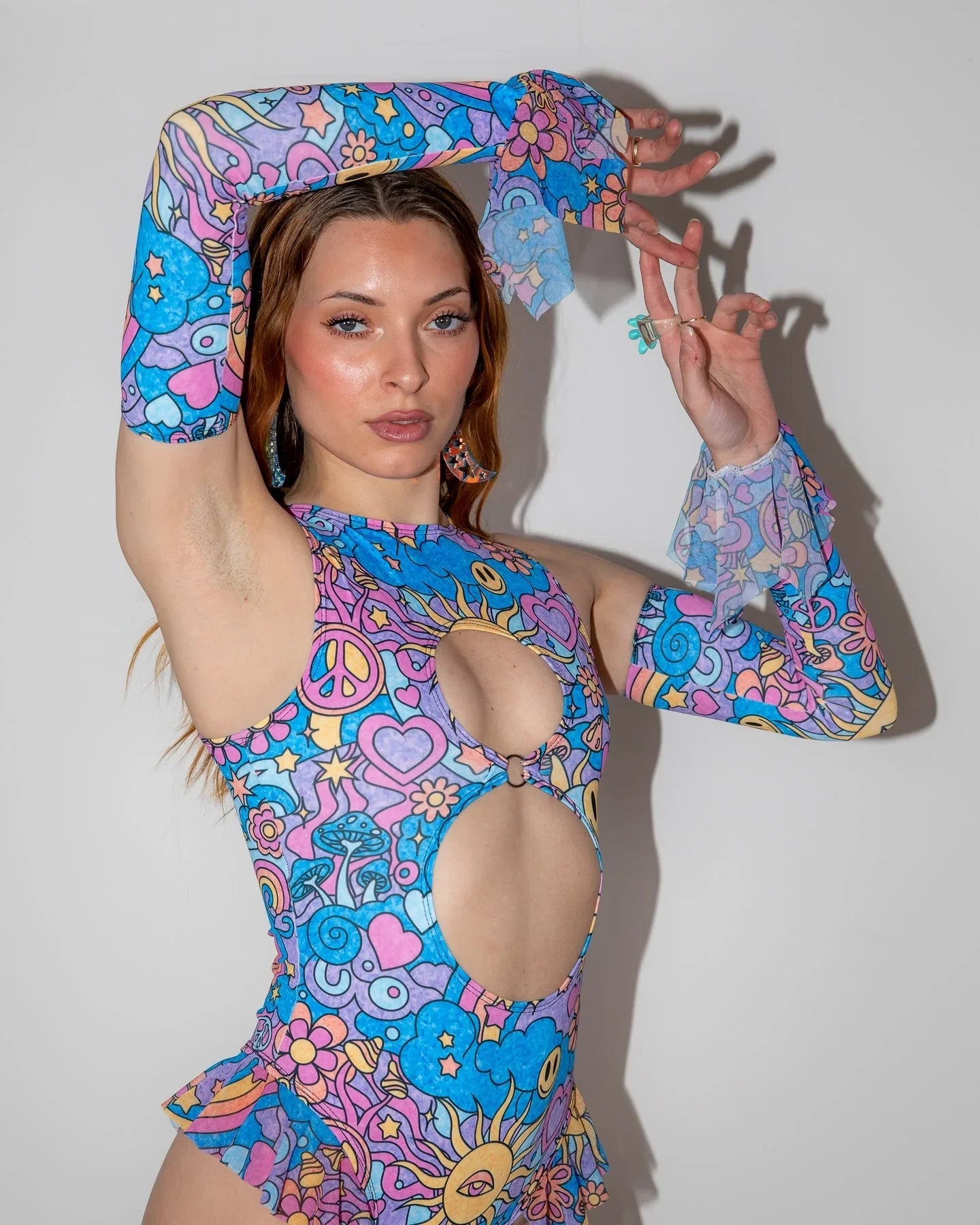 Front view of Groovy Spellcaster Arm Sleeves on a model, showcasing the pastel psychedelic rave pattern with peace signs and hearts.
