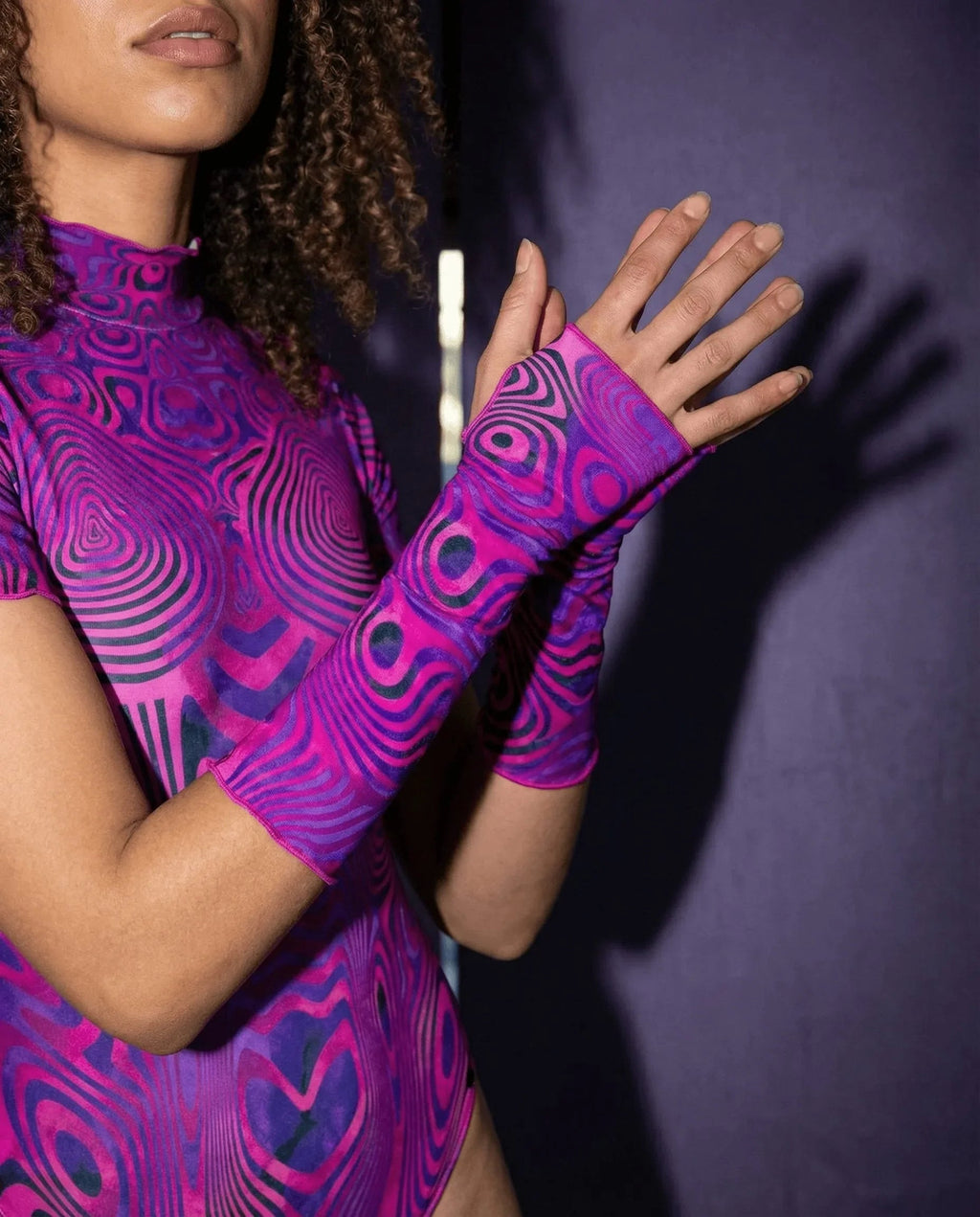 A model wearing Vanish Gloves, magenta and violet rave arm sleeves, with a matching top, hands raised in a lifestyle shot.