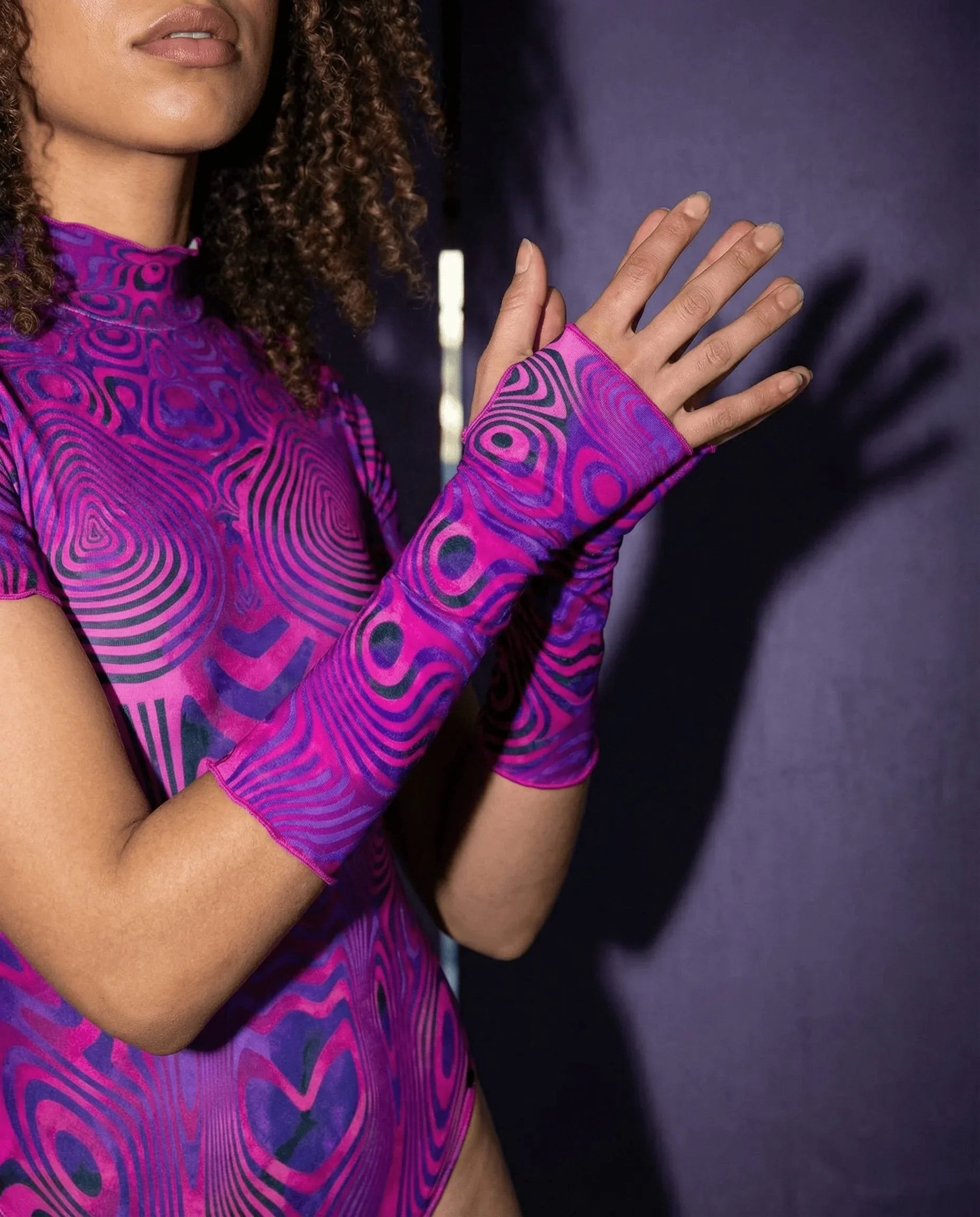 A model wearing Vanish Gloves, magenta and violet rave arm sleeves, with a matching top, hands raised in a lifestyle shot.