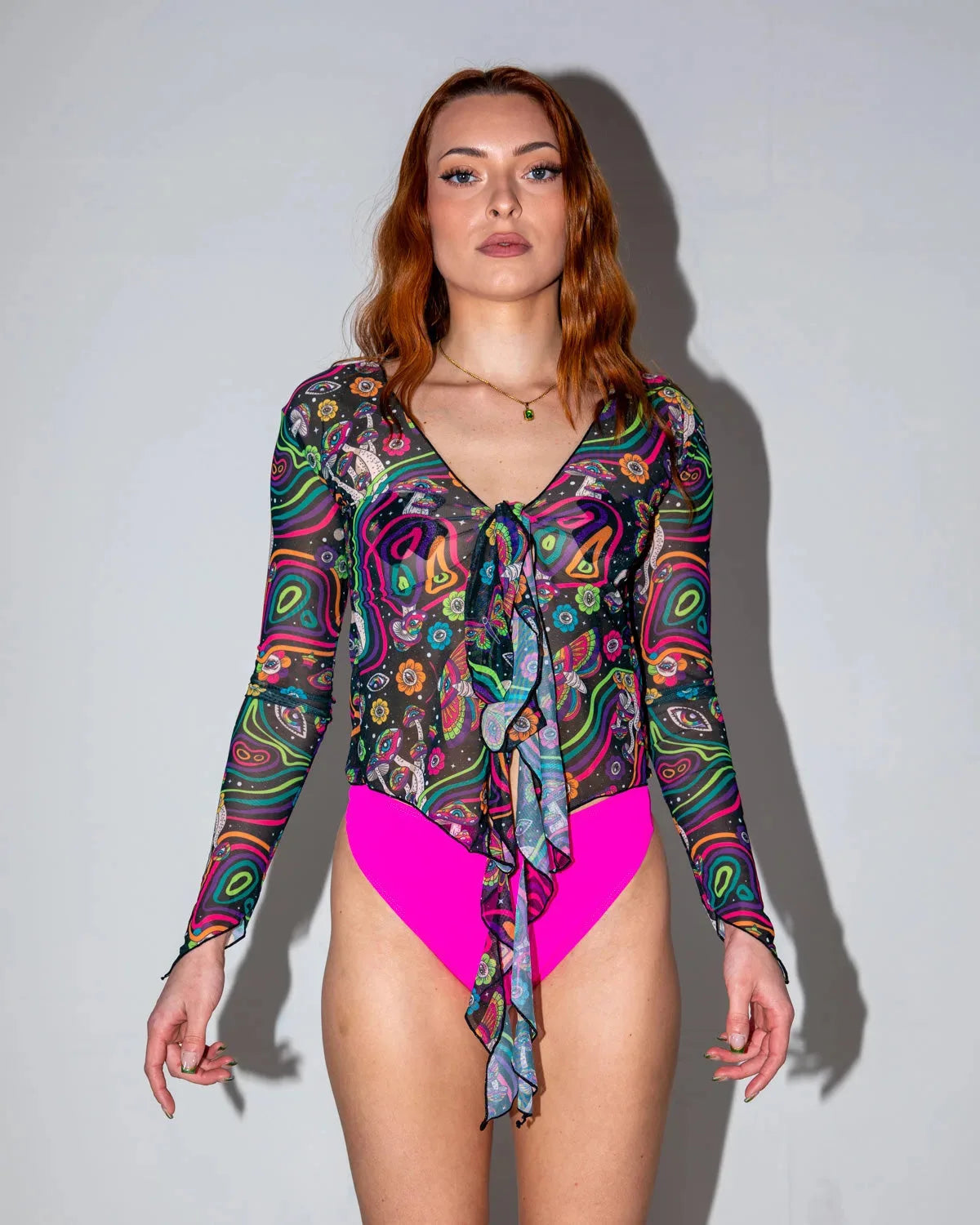 Awaken Sea Fairy Tie Top shown from the front on a model, featuring a sheer, long-sleeved, psychedelic multi-color rave top over a pink bodysuit.