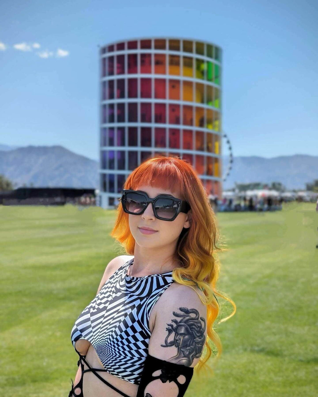 Woman modeling black white geometric rave top with distortion print at outdoor festival venue with colorful architecture