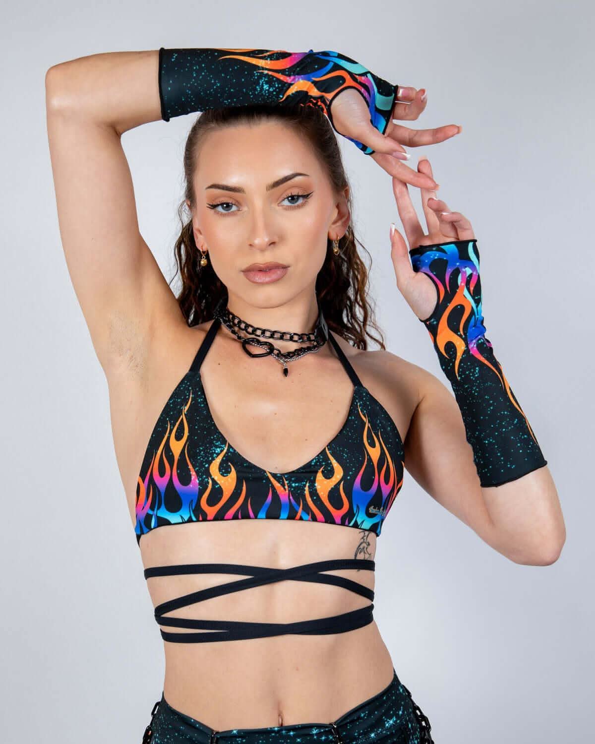 Model wearing Blaze flame print rave top with matching arm sleeves in vibrant multicolored flames against black sparkly fabric