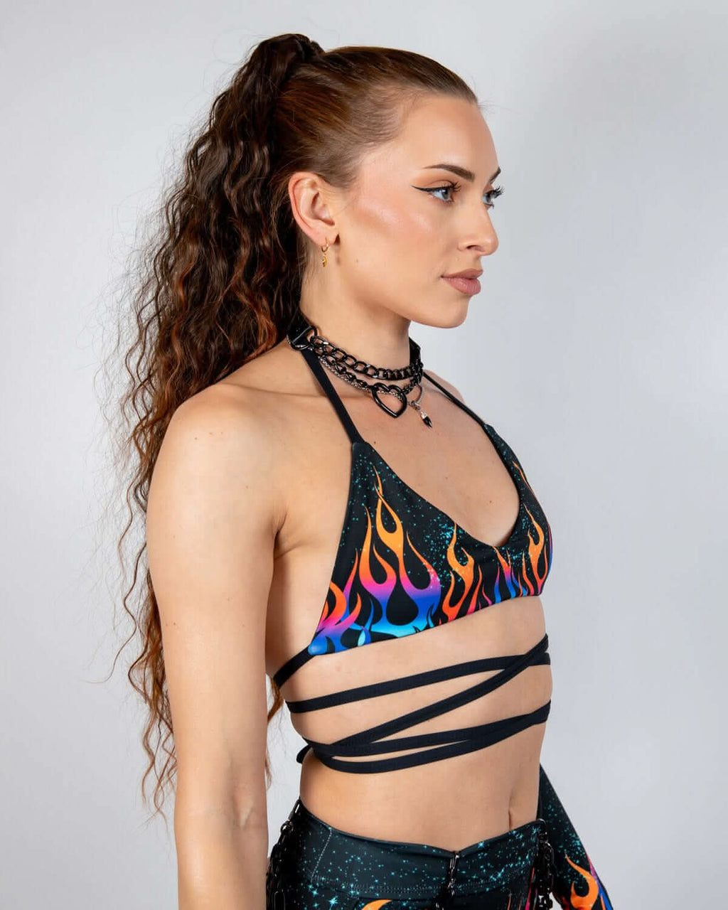 Profile view of model wearing Blaze flame print rave top with wraparound straps and chain choker