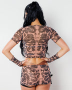 Dynasty Baby Tee in nude, seen from the back on a model, featuring intricate black dragon print for rave festivals.