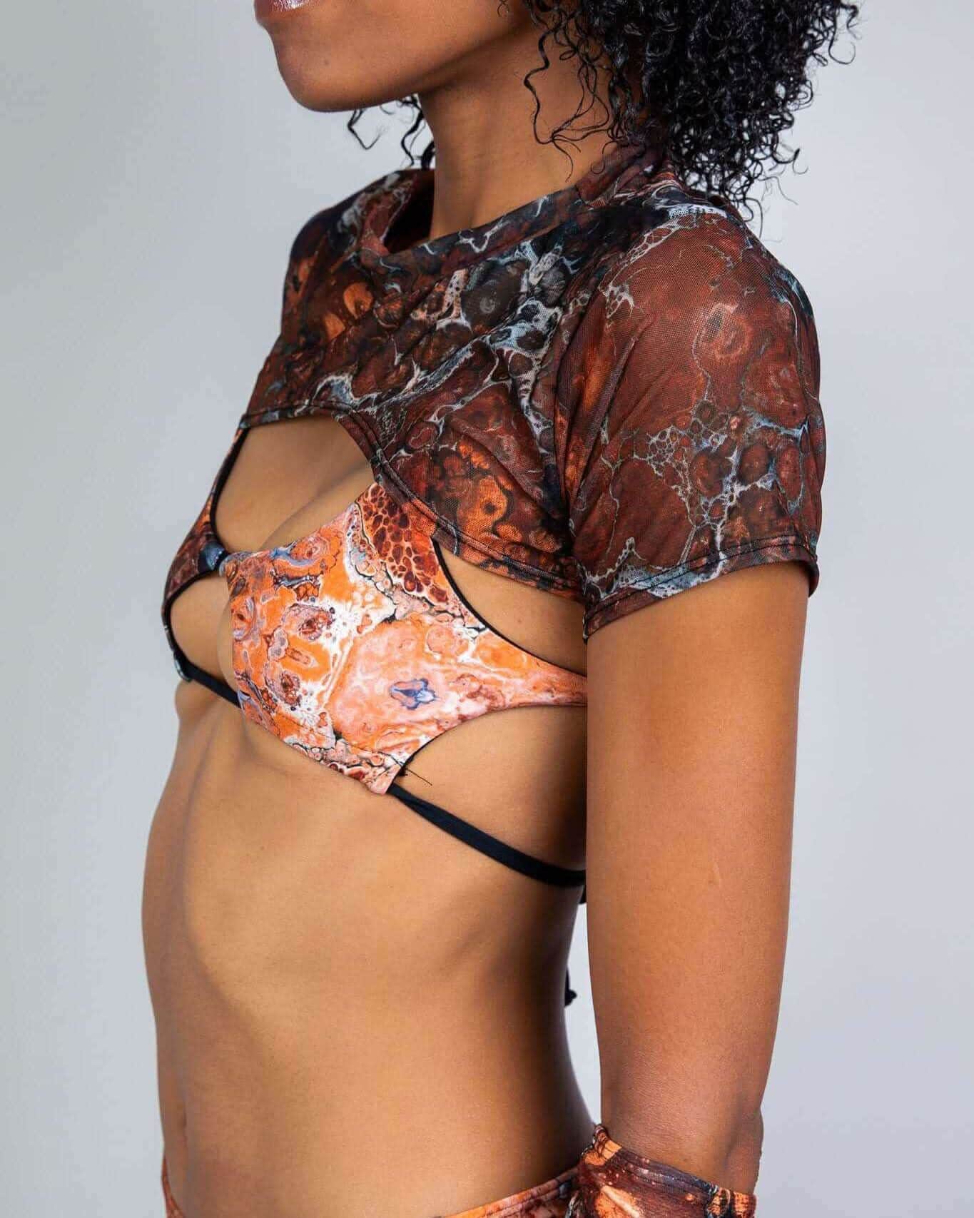 Side view of model wearing Fossil marbled mesh rave top with cap sleeves over orange patterned bra