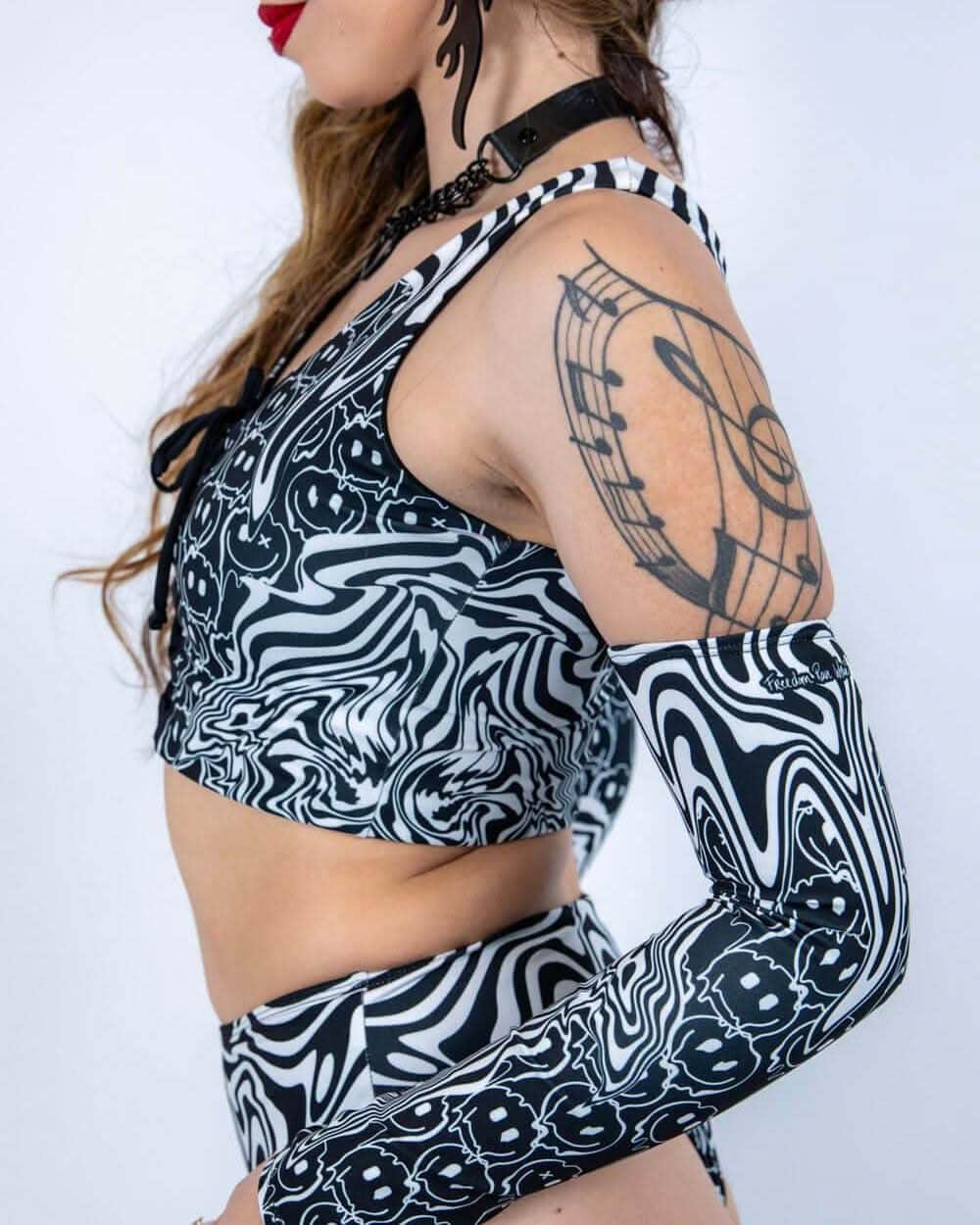 Side view of model wearing black white Meltdown psychedelic rave top with matching arm sleeves showing music tattoo