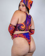 Plus-size model wearing Radiance rave top with electric orange and purple swirl patterns, back view