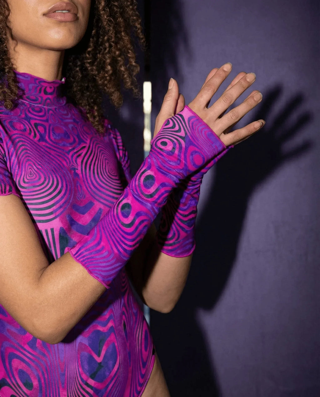 Model showcasing pink purple Vanish pattern rave arm sleeves in dynamic pose with raised hand