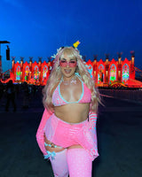 Person in neon pink wrap bikini top enjoying a rave with vibrant lights in the background, showcasing festival fashion.