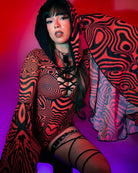 Woman in a red patterned bodysuit with dramatic sleeves, showcasing a stylish rave outfit.
