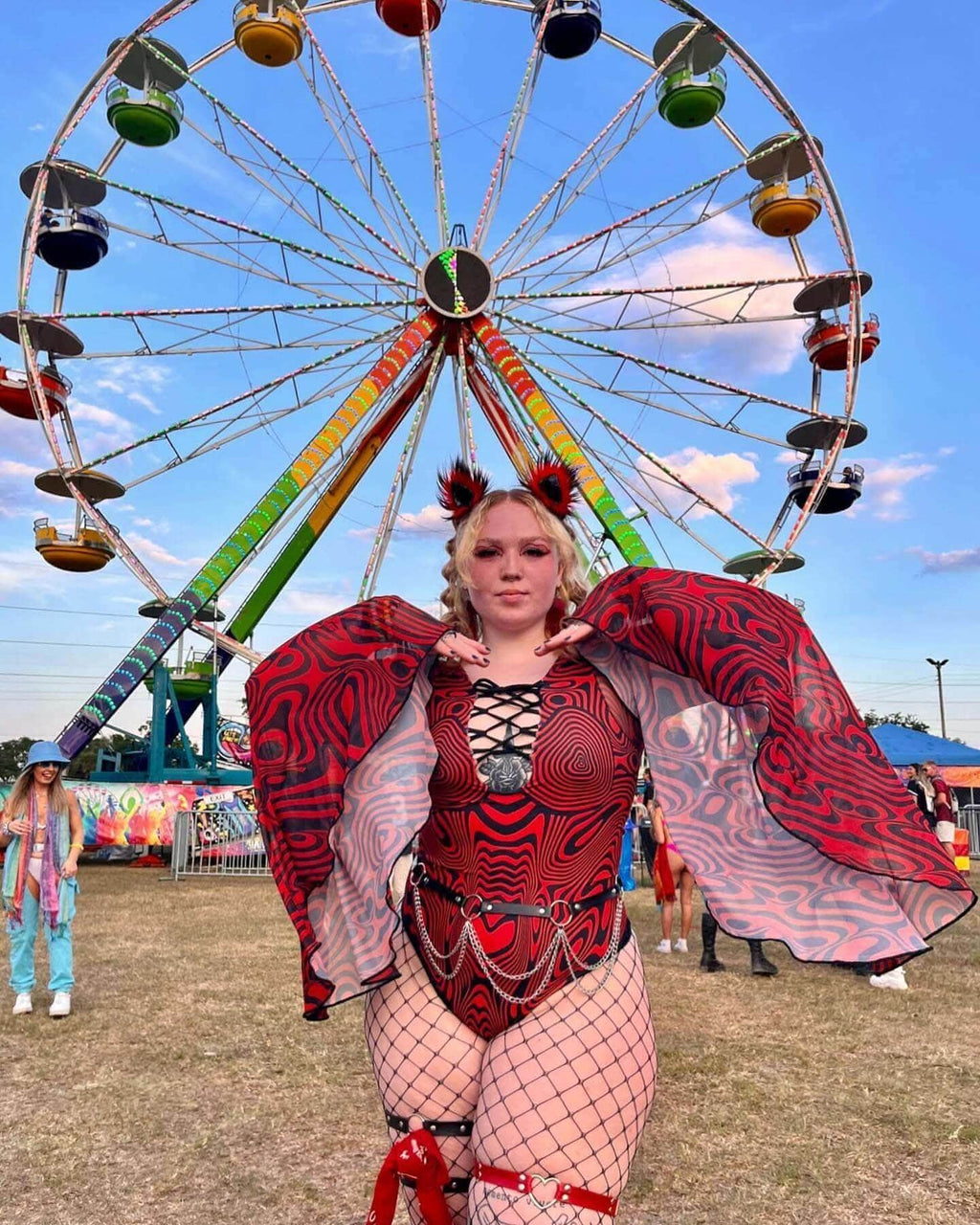Woman in a vibrant Red Void Goddess Bodysuit poses in front of a colorful ferris wheel, showcasing rave outfits.