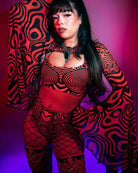Model in psychedelic red and black outfit with bell sleeves, perfect for rave outfits, posed under colorful lighting.