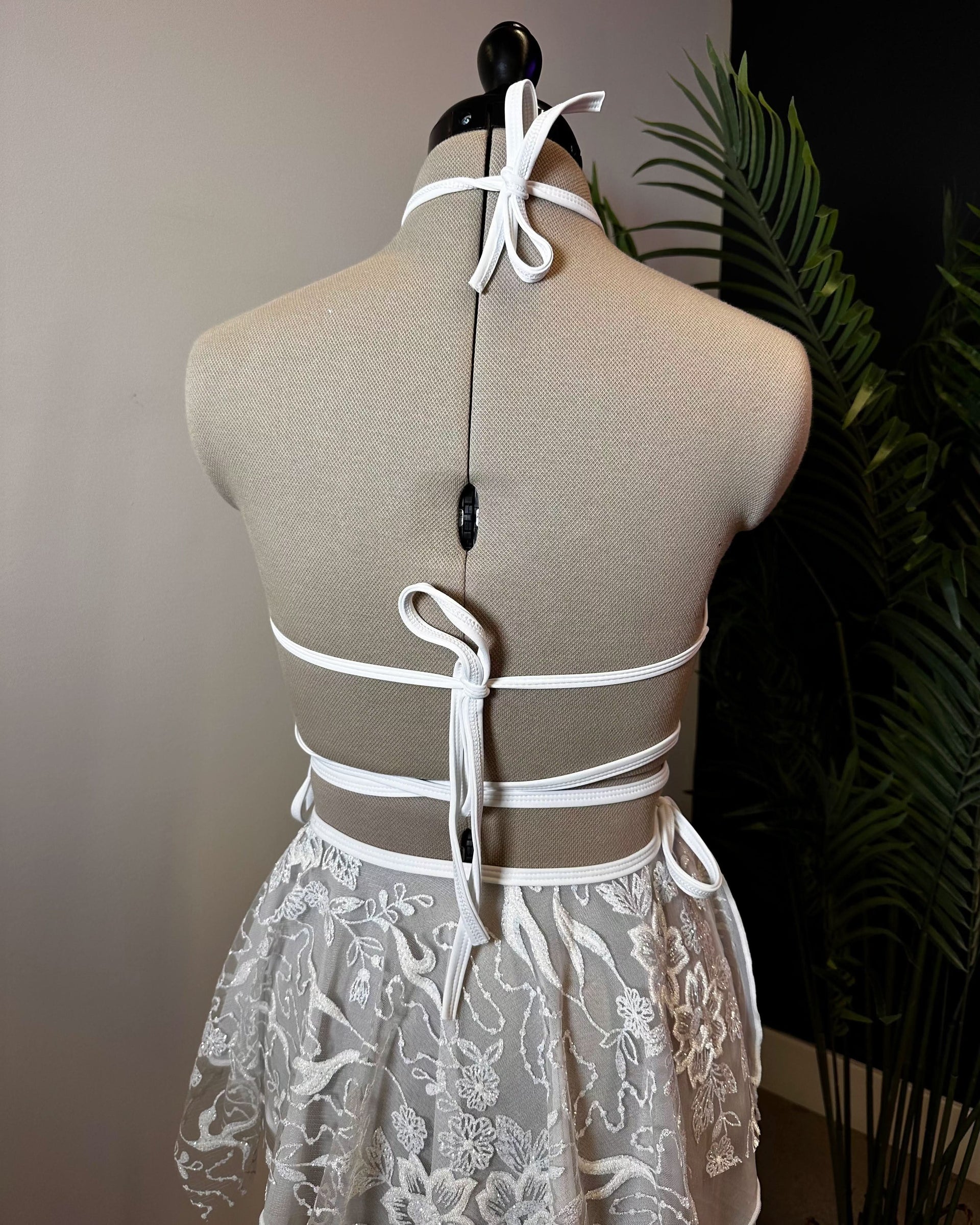 Back view of white Seraphina Wrap rave top with ribbon ties on dress form with lace skirt