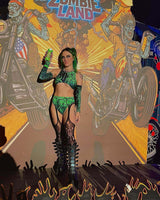 Model in green toxic rave outfit poses with a drink in front of a vibrant Zombie Land backdrop.