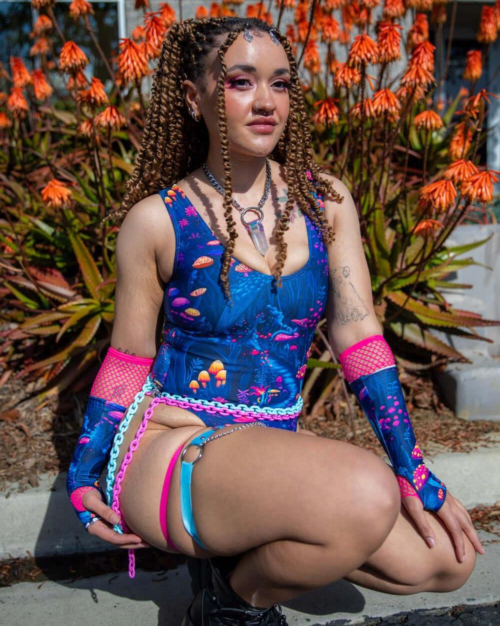 Model sitting outdoors wearing the Wildwood Classic Bodysuit, featuring an Alice in Wonderland-inspired print.