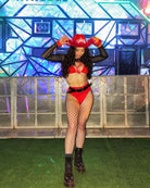 Model in a red bikini, fishnet stockings, and black mesh long sleeves, posing in a colorful rave setting.