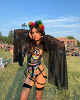 Model in vibrant rave outfit with black mesh bell sleeves and colorful accessories at a festival.