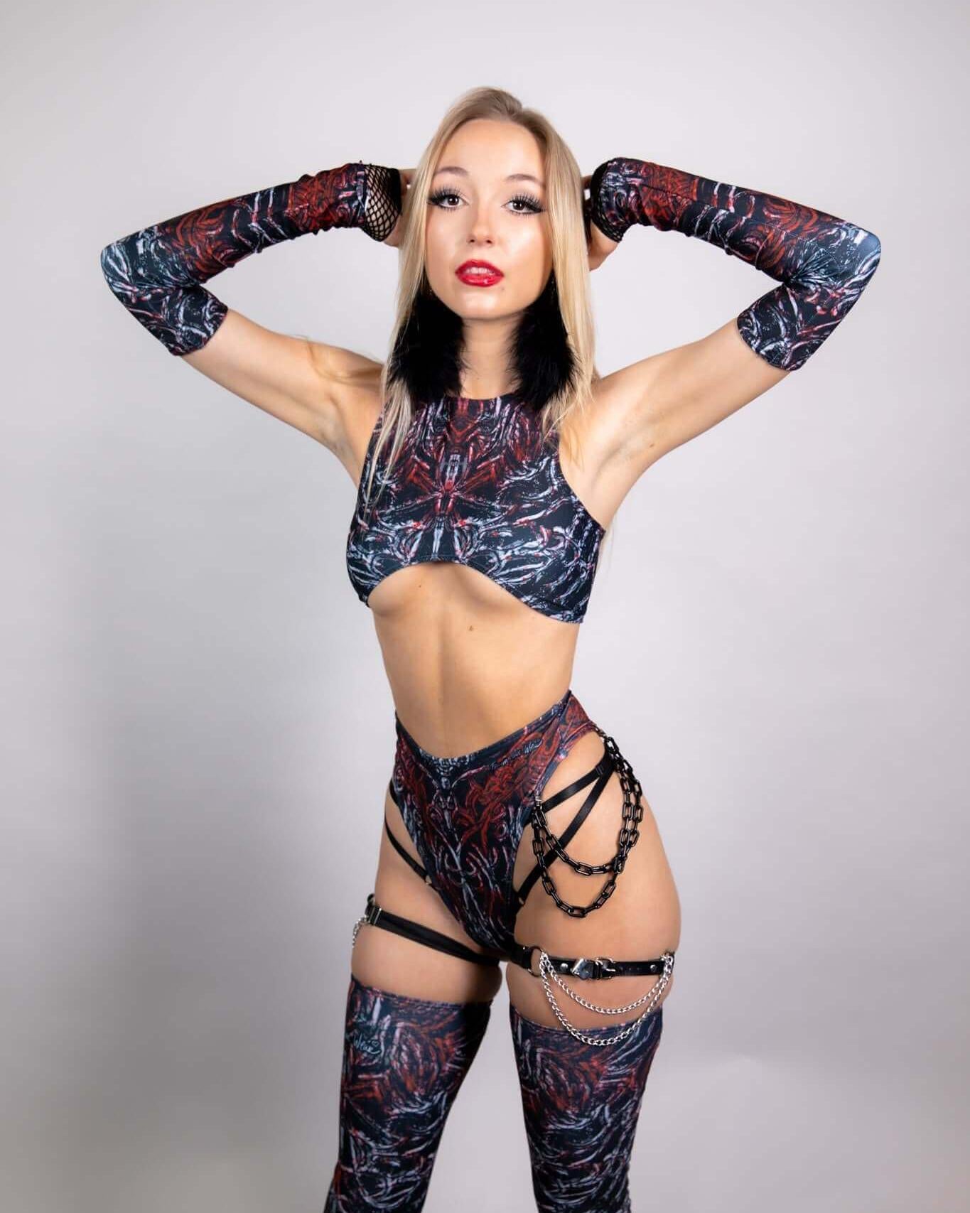 Model showcasing a stylish rave outfit with a black and red pattern, featuring gloves and harness-style accessories.