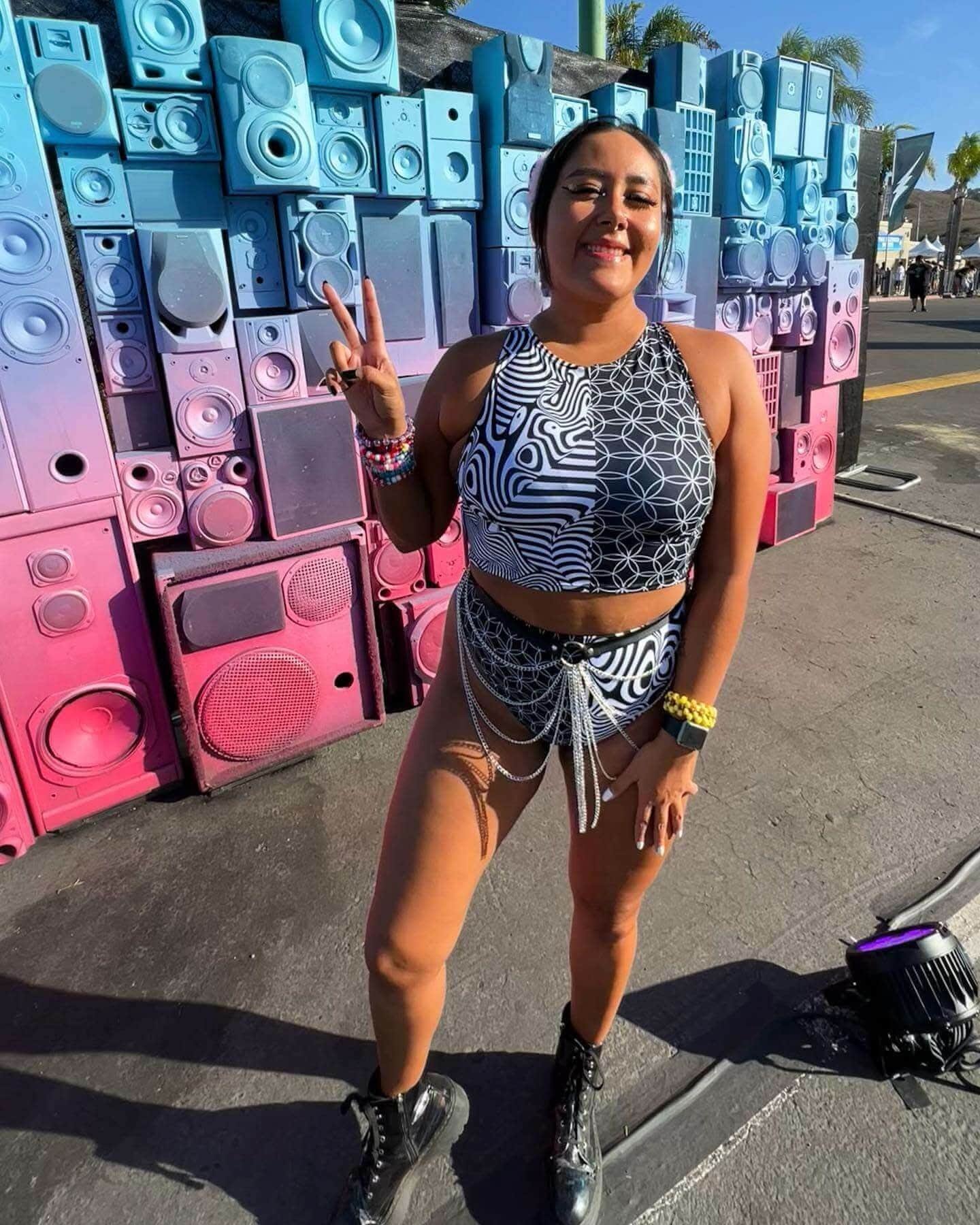Woman wearing Duality High Waisted Brazilian Bottoms with a trippy black and white pattern at a vibrant festival backdrop.