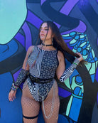 Woman wearing Duality Sideboob Bodysuit with black and white patterns, posing in front of a colorful mural, ideal for rave outfits.