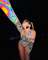 Woman in colorful HAPPIER Arm Sleeves and trippy bodysuit, showcasing vibrant rainbow design perfect for rave outfits.