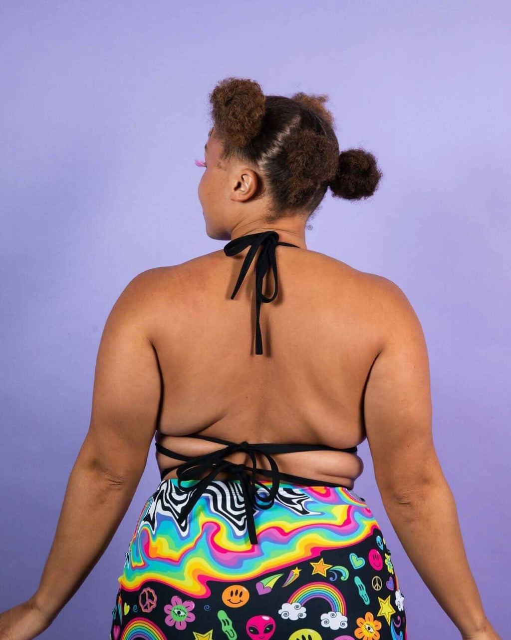 Back view of a model wearing the HAPPIER Extra Mile Bralette with trippy rainbow print and criss-cross straps. Perfect for rave outfits.