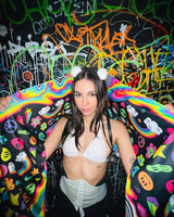 Model showcasing the HAPPIER Festival Scarf with trippy rainbow design against a vibrant graffiti background. Perfect for rave outfits.