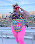 Trendy plus-size model in a colorful rainbow sideboob bodysuit at a vibrant EDM festival, showcasing bold rave outfits.
