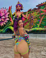 Woman in a colorful sideboob bodysuit poses at an EDM festival with vibrant art behind her, showcasing rave outfits.