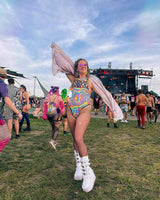 Vibrant woman in psychedelic rainbow bodysuit at EDM festival, showcasing trendy rave outfits and summer festival fun.