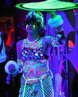 Model in a colorful, psychedelic bodysuit performing at an EDM festival, showcasing vibrant rave fashion.