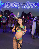 Young woman wearing a colorful rave outfit at an EDM festival under the "Daisy Lane" neon sign.