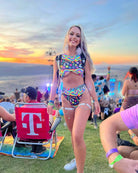 Young woman in a trippy rainbow crop top and shorts at a rave, showcasing the vibrant EDM fashion in a festival setting.