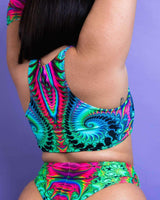Woman showcasing vibrant Hypnotic Teaser top and matching bottoms, perfect for rave outfits, against a purple background.