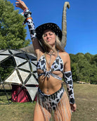 Woman in a black and white cow print bikini and hat dancing at a rave, showcasing fun festival fashion.