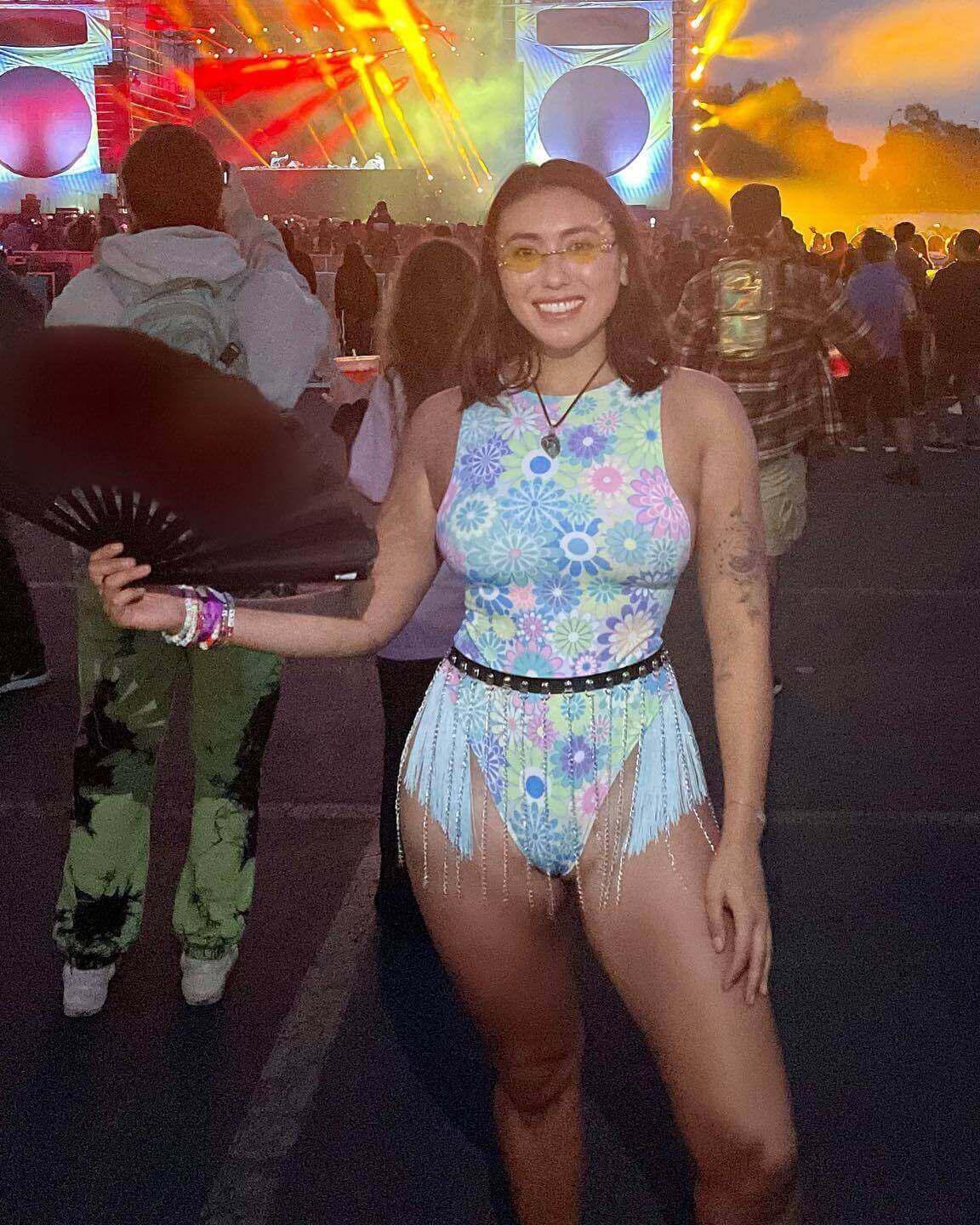 Woman in colorful rave outfit with fringe and fan at a vibrant music festival, showcasing stylish festival fashion.