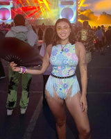 Woman in colorful rave outfit with fringe and fan at a vibrant music festival, showcasing stylish festival fashion.