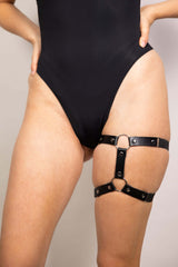 Black leather adjustable leg garter worn with a sleek black bodysuit, perfect for edgy rave outfits.