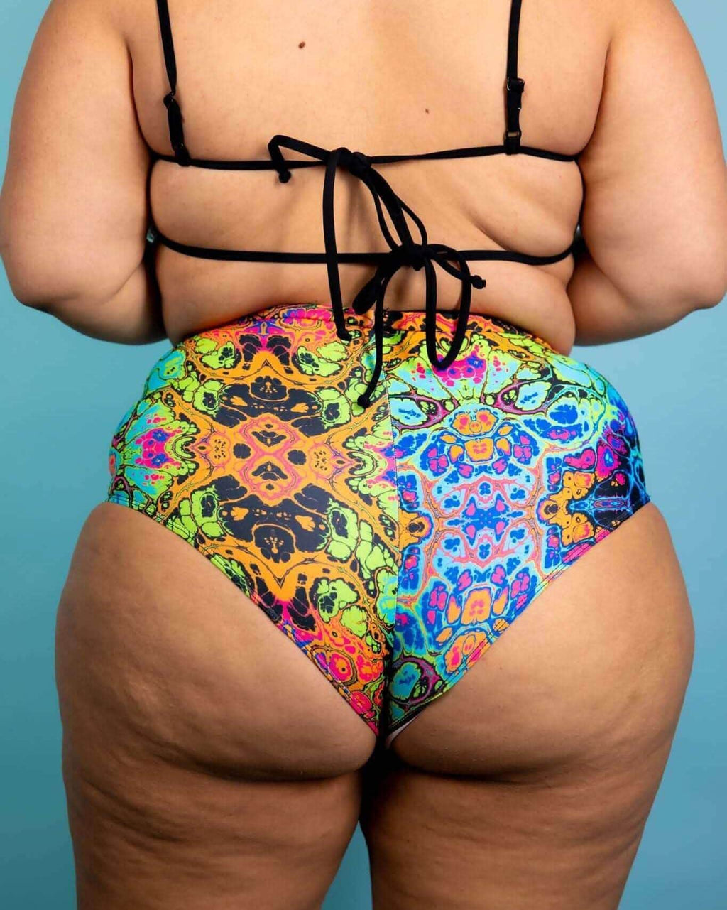 Back view of Lucidity High Waisted Brazilian Bottoms featuring a psychedelic rainbow design, perfect for rave outfits.
