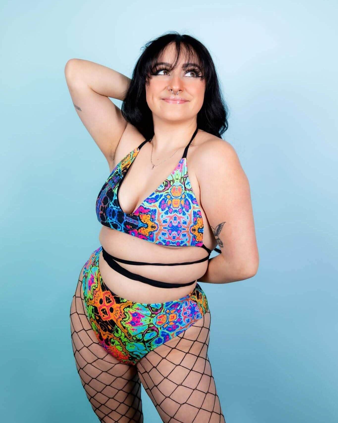 Model wearing Lucidity High Waisted Brazilian Bottoms with psychedelic rainbow design, perfect for rave outfits.