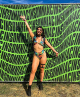 raver wears color bright psychedelic two piece rave outfit in front of green and black backdrop