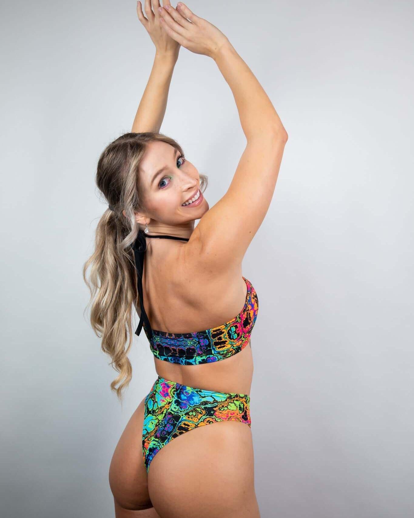 Model showcasing the Lucidity High Waisted Thong in a vibrant psychedelic rainbow design, ideal for rave outfits.