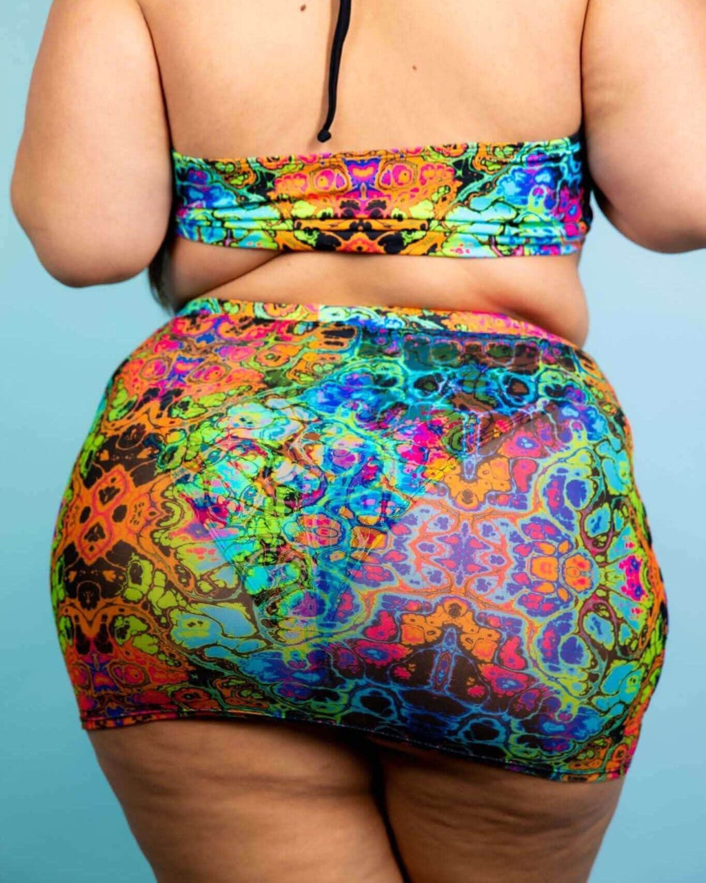 Plus-size model wearing a psychedelic rainbow design mini skirt, perfect for rave outfits and festivals.
