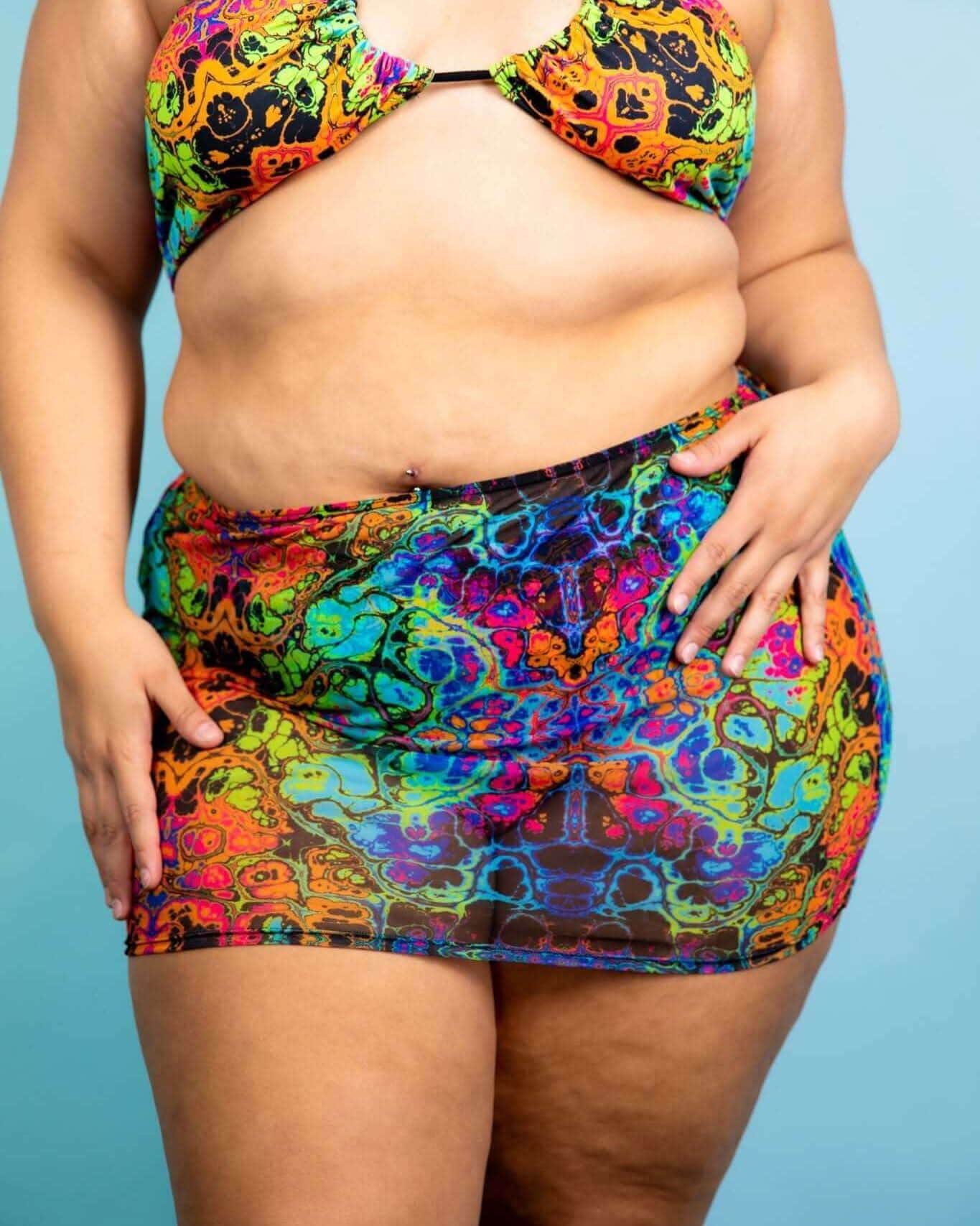 Model wearing Lucidity Mesh Extra Mini Skirt with psychedelic rainbow design, perfect for rave outfits and festival looks.